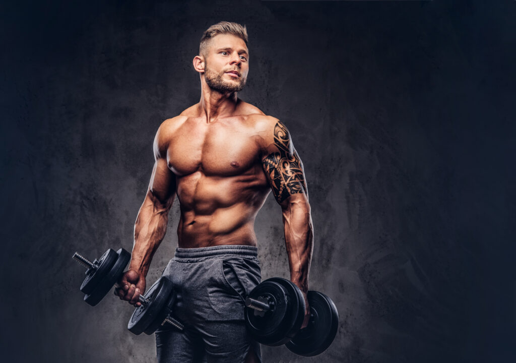 Handsome shirtless tattooed bodybuilder wearing sports shorts, posing in a studio.